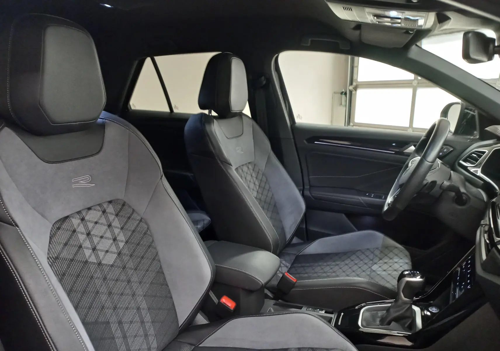 Vue intérieure côté conducteur du Volkswagen T-Roc 1.5 TSI R-Line 2025, sièges sport en tissu et alcantara gris avec logo R.