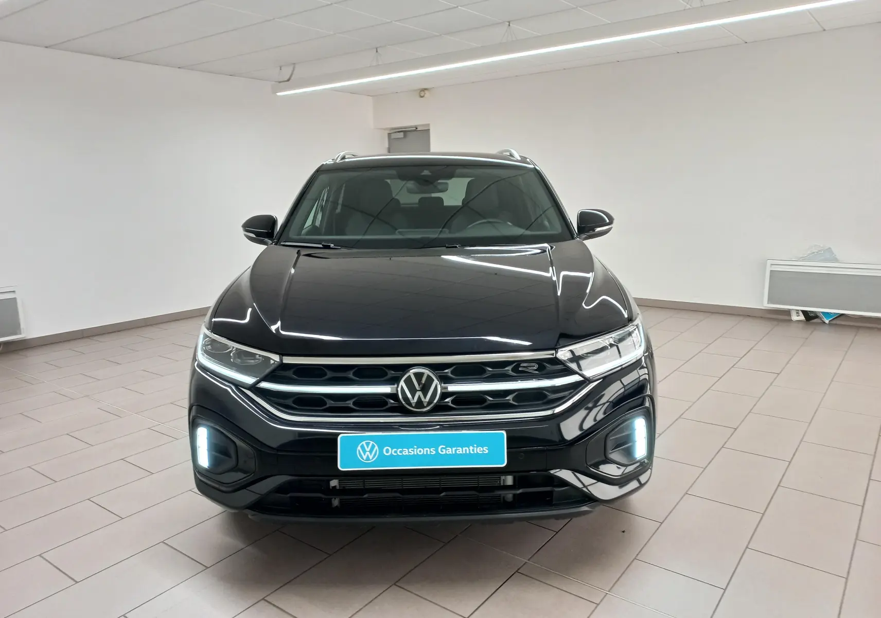 Vue de face du Volkswagen T-Roc 1.5 TSI 150 DSG7 R-Line noir intense nacré avec feux LED allumés en intérieur.