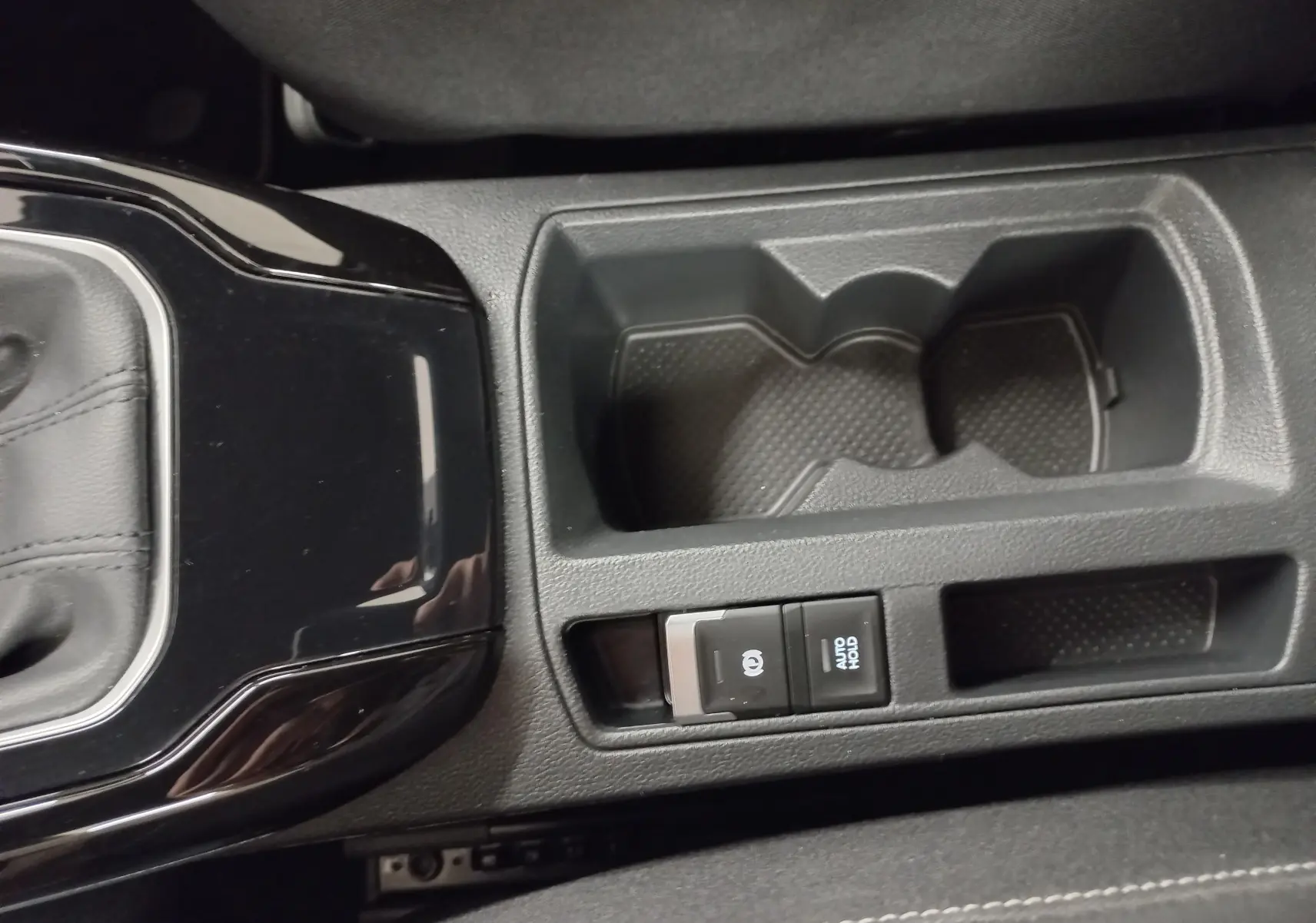 Gros plan sur la console centrale noire du Volkswagen T-Roc 2025, avec porte-gobelets et boutons frein à main électronique et Auto Hold.