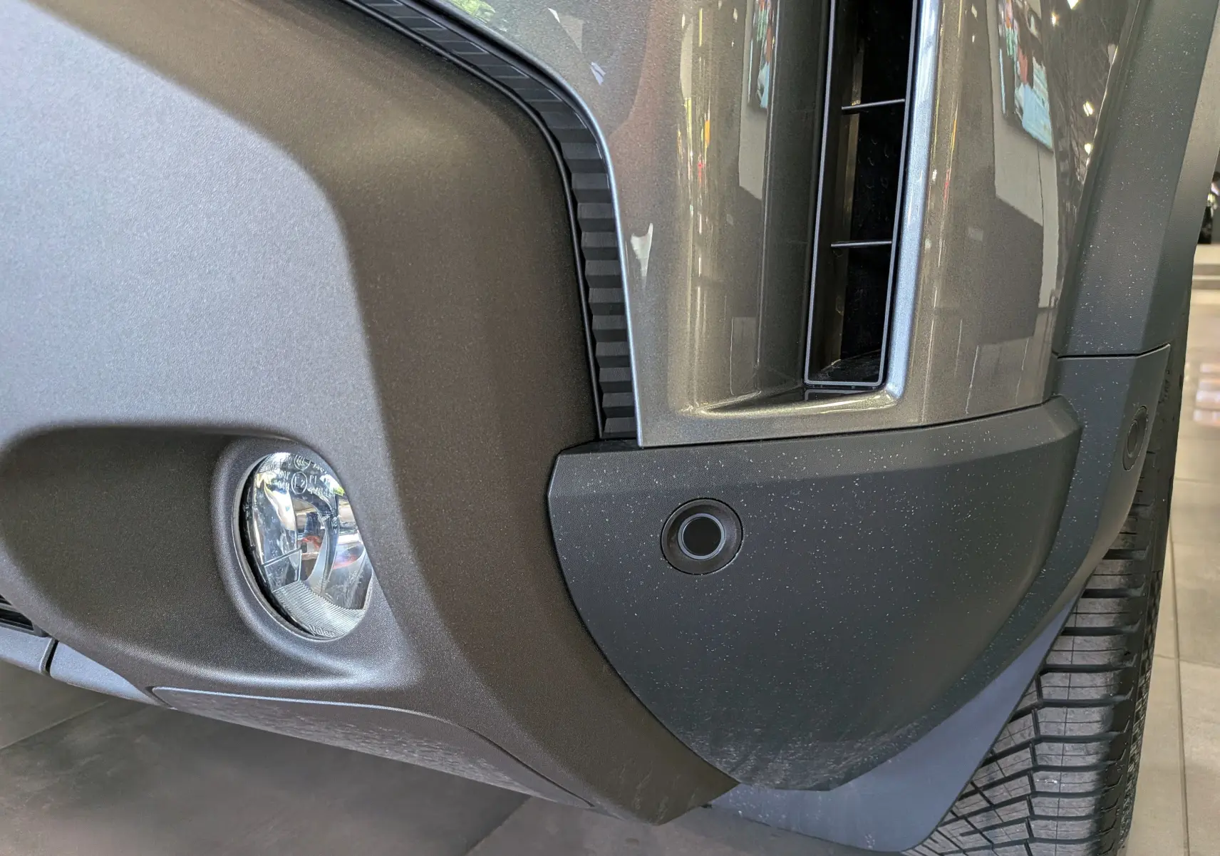 Gros plan sur le pare-chocs avant droit gris schiste du Dacia Duster Hybrid-G 150 CH 4x4 avec antibrouillard et capteur de stationnement.
