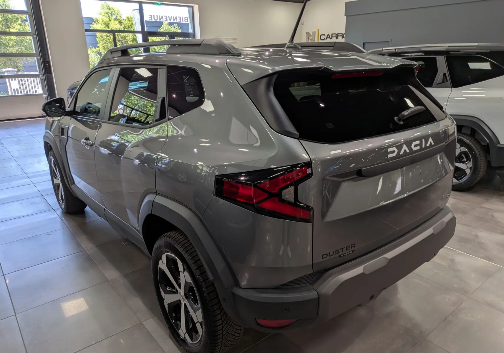 Vue 3/4 arrière droite du Dacia Duster Hybrid-G gris schiste avec jantes biton et feux arrière LED distinctifs en showroom.