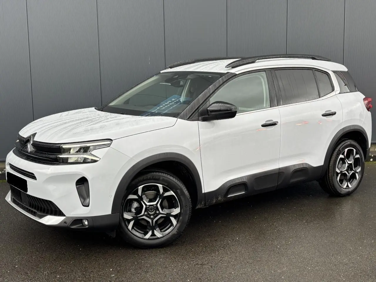 Vue 3/4 avant droite d'un Citroën C5 Aircross blanc Okénite avec jantes alliage bi-ton et barres de toit noires.