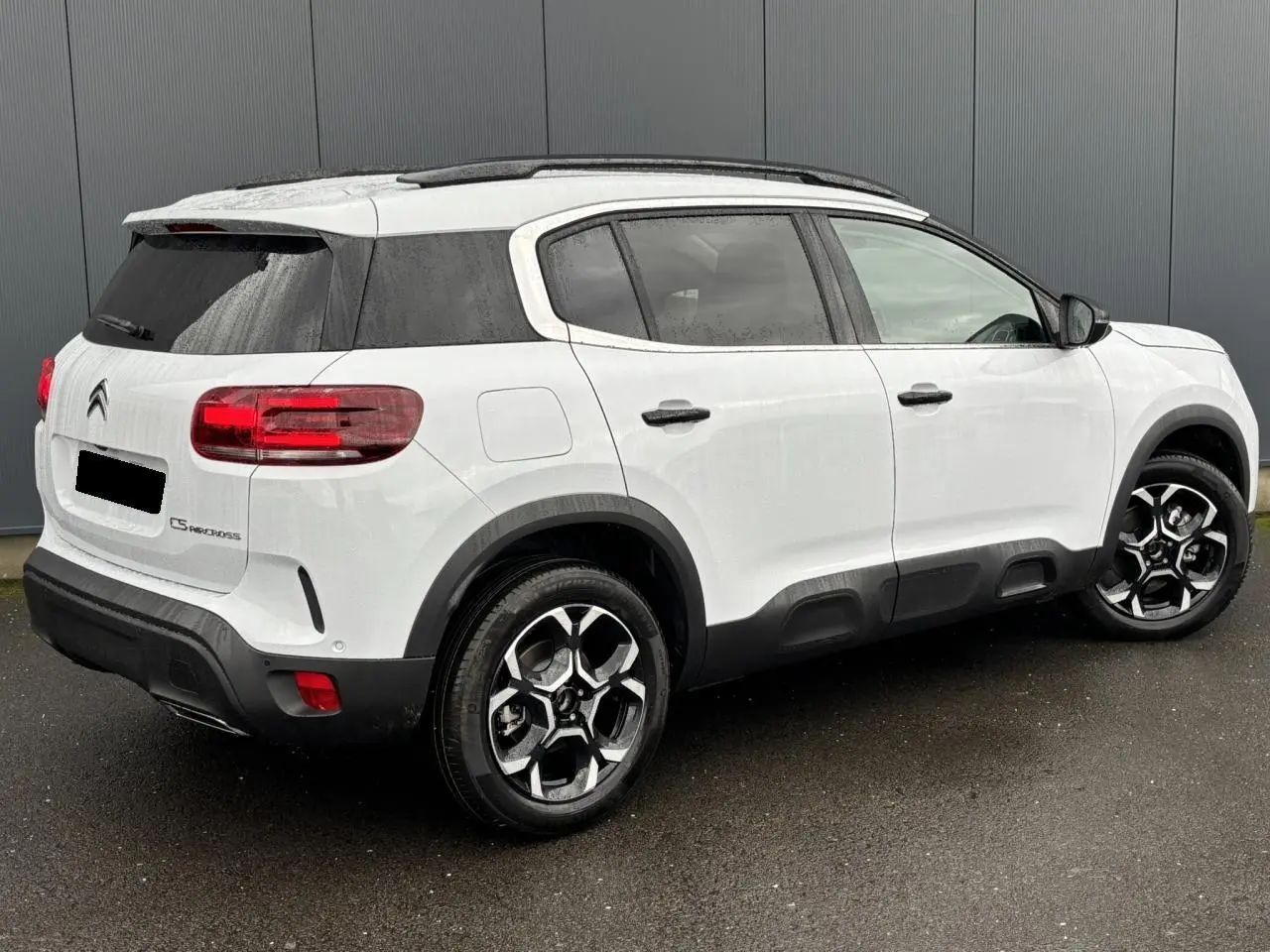 Vue 3/4 arrière droite d’un Citroën C5 Aircross blanc Okénite avec jantes alliage bi-ton et barres de toit noires.