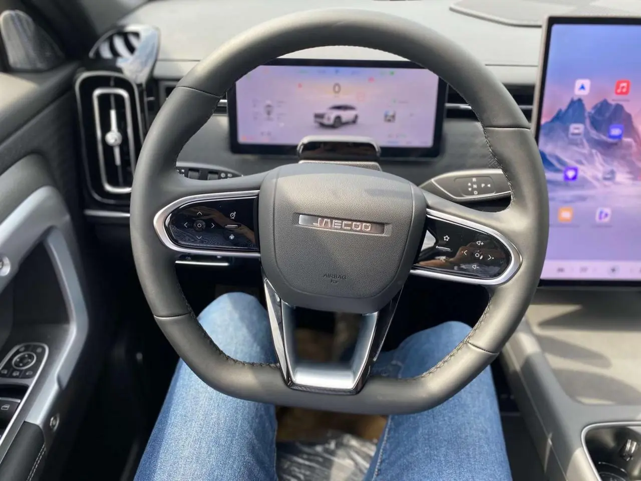 Vue intérieure centrée sur le volant JAECOO avec tableau de bord numérique et écran tactile latéral.