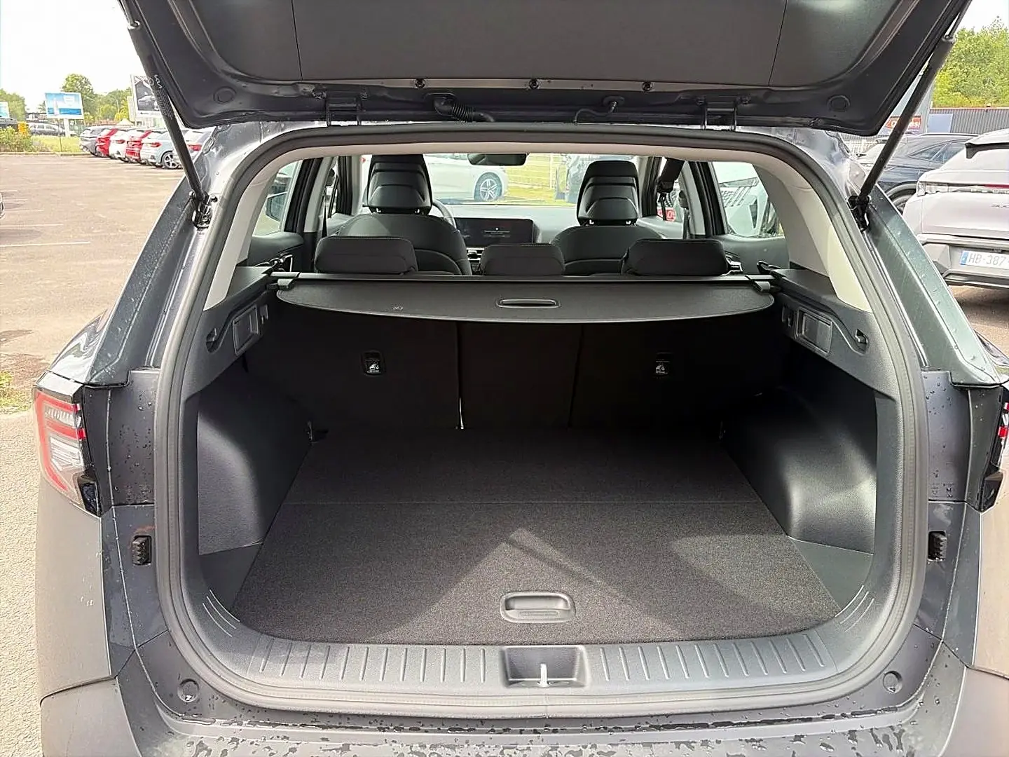 Coffre ouvert vu de l'arrière d'un KIA Sportage 1.6 hybride gris eclipse avec cache-bagages et banquette arrière visible.