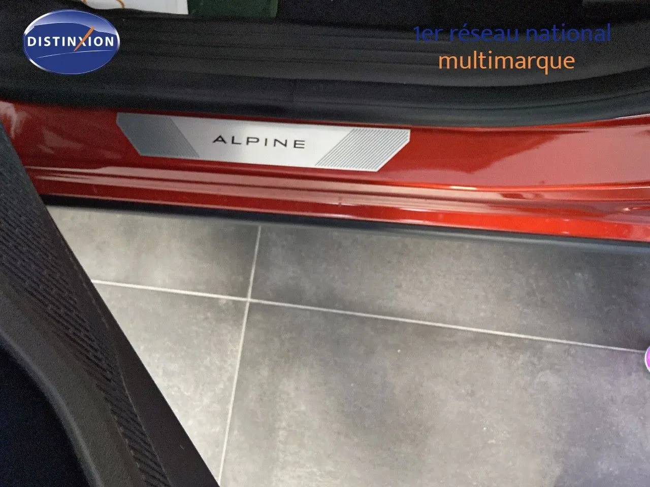 Gros plan sur la plaque Alpine rouge flamme métal visible à l'entrée côté gauche de la Renault Rafale 2024.