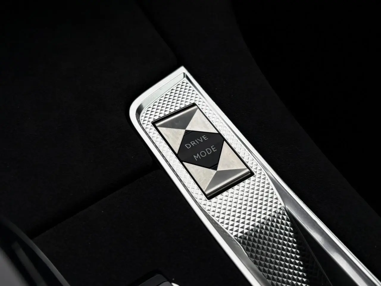 Gros plan sur le sélecteur de mode de conduite en métal brossé dans la console centrale noire du DS7 gris laqué.