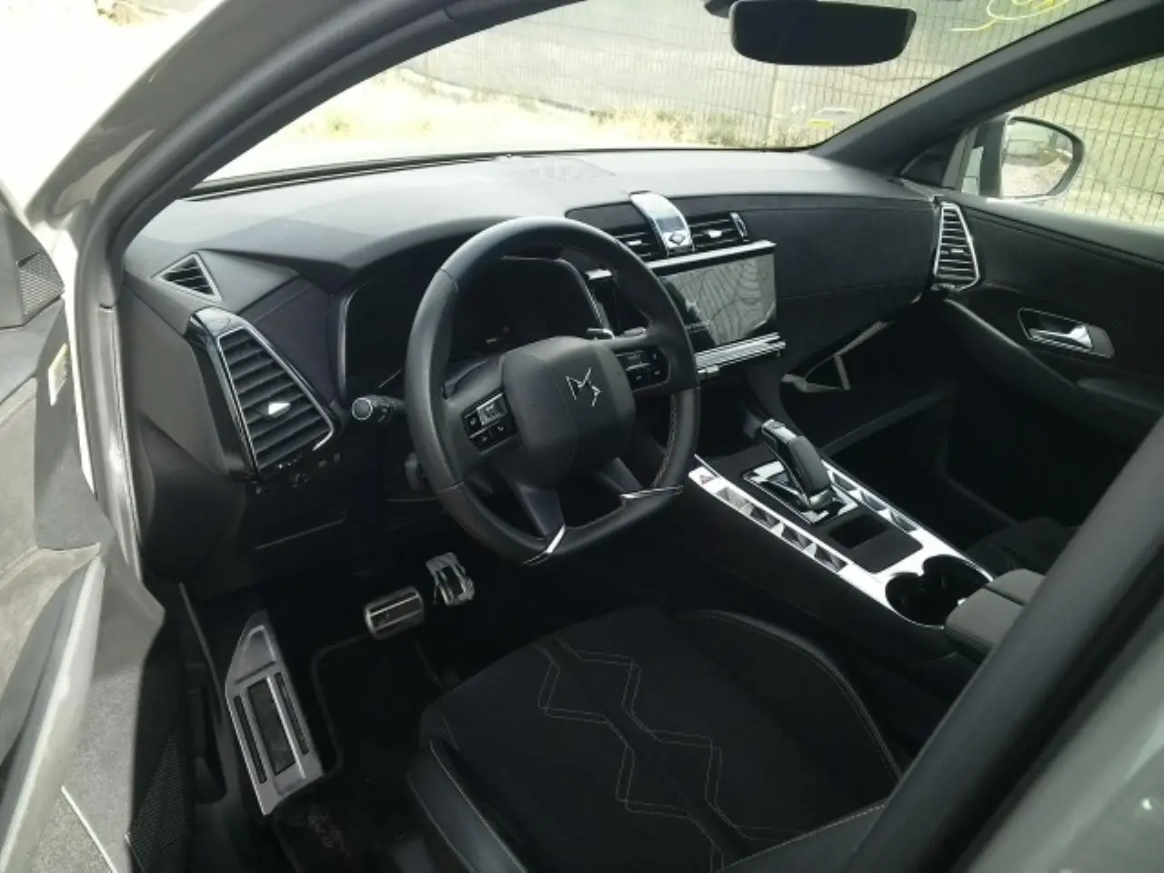 Vue intérieure côté conducteur du DS7 2024 gris laqué, mettant en valeur le volant cuir, la console centrale brillante et l'écran tactile.