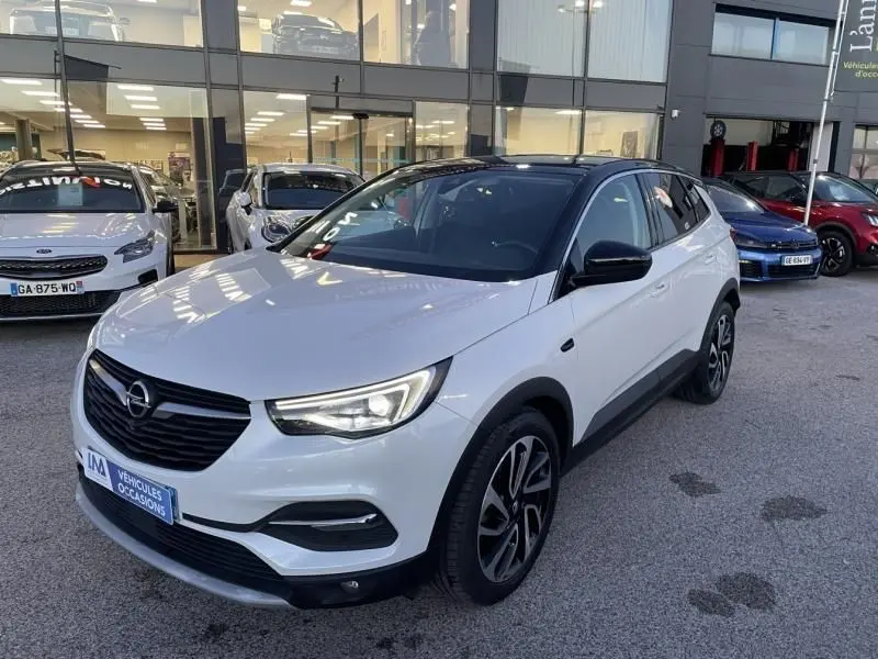 Opel Grandland X blanc avec toit noir, vue 3/4 avant droit, calandre noire et jantes alliage distinctives.