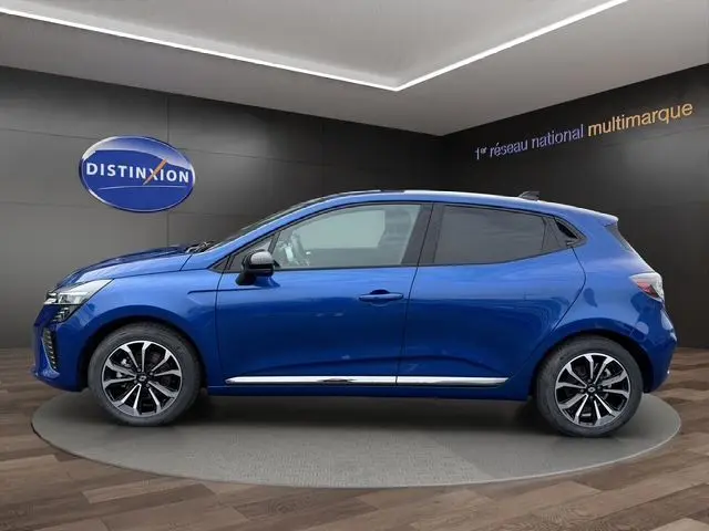 Profil droit d'une Renault Clio V E-Tech Full Hybrid 145ch en bleu Iron avec jantes alliage noires sur fond showroom.