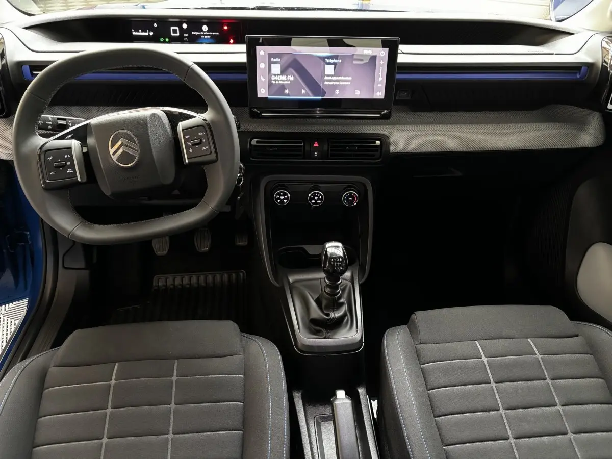 Vue intérieure avant de la Citroën C3 100 BVM PLUS 2025 bleue, avec volant cuir, écran tactile central et levier de vitesse manuel.