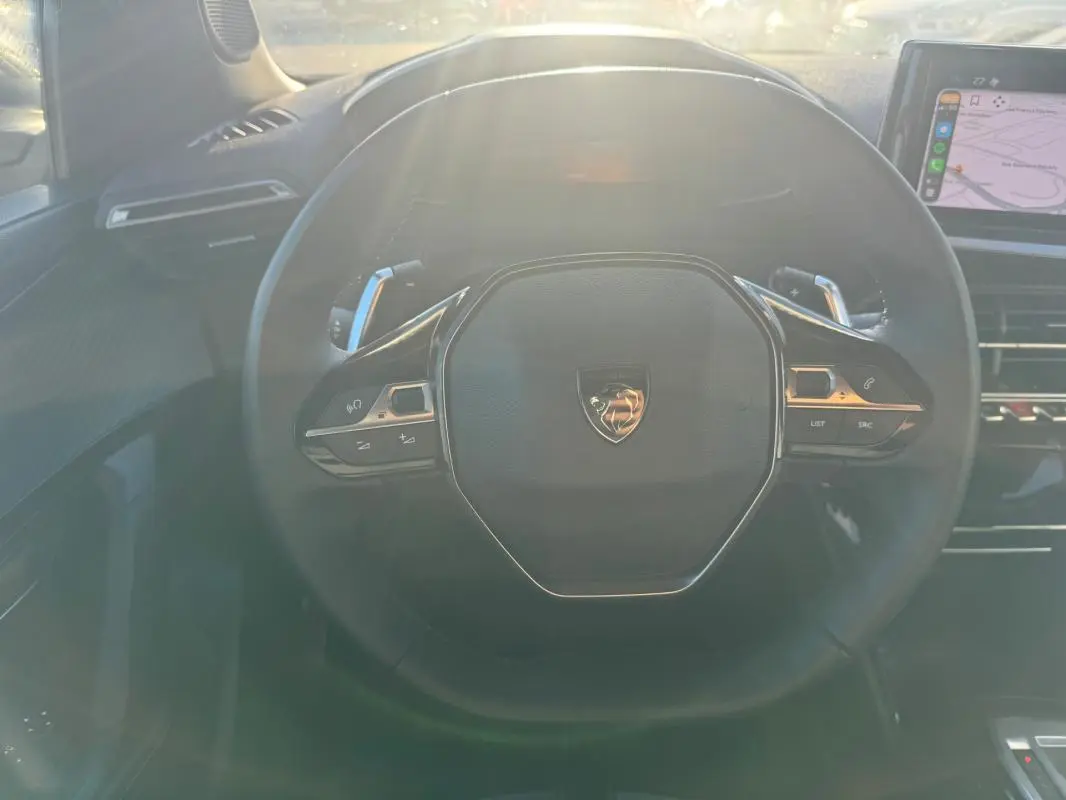 Vue rapprochée du volant noir du Peugeot 2008 Hybrid 136 e-DCS6 Allure 2024 avec commandes intégrées et écran tactile visible.