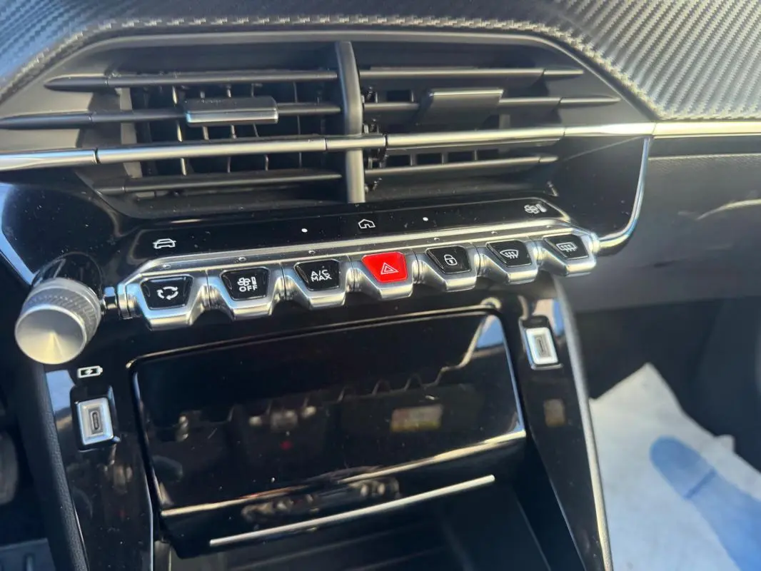 Vue rapprochée de la console centrale noire brillante du Peugeot 2008 Hybrid 136 avec boutons de commande et prise USB.