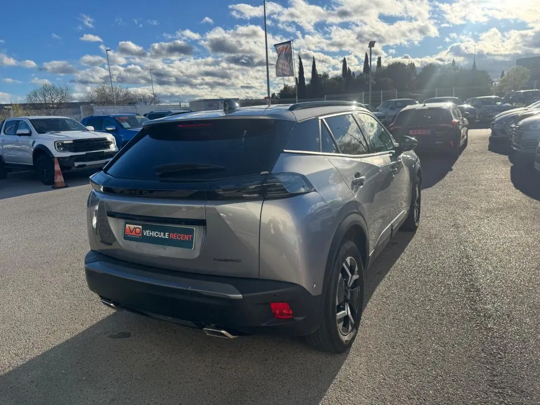 Vue 3/4 arrière droite d’un Peugeot 2008 Hybrid gris 2024 avec barres de toit et jantes alliage 17 pouces.