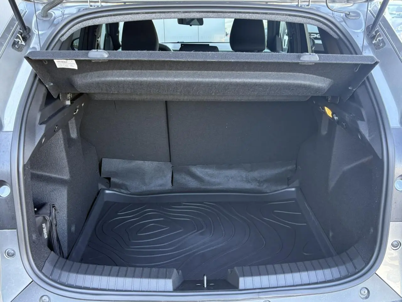 Coffre ouvert vu de l'arrière du Dacia Duster Gris Schiste 2026, avec tapis de coffre noir et habillage intérieur sombre.