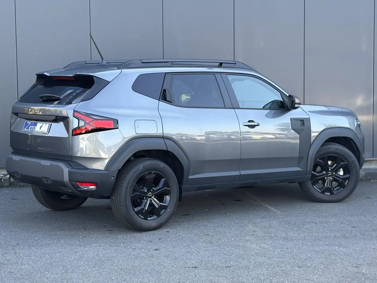 Vue latérale droite du Dacia Duster 2026 gris schiste avec jantes alliage noires et barres de toit longitudinales.
