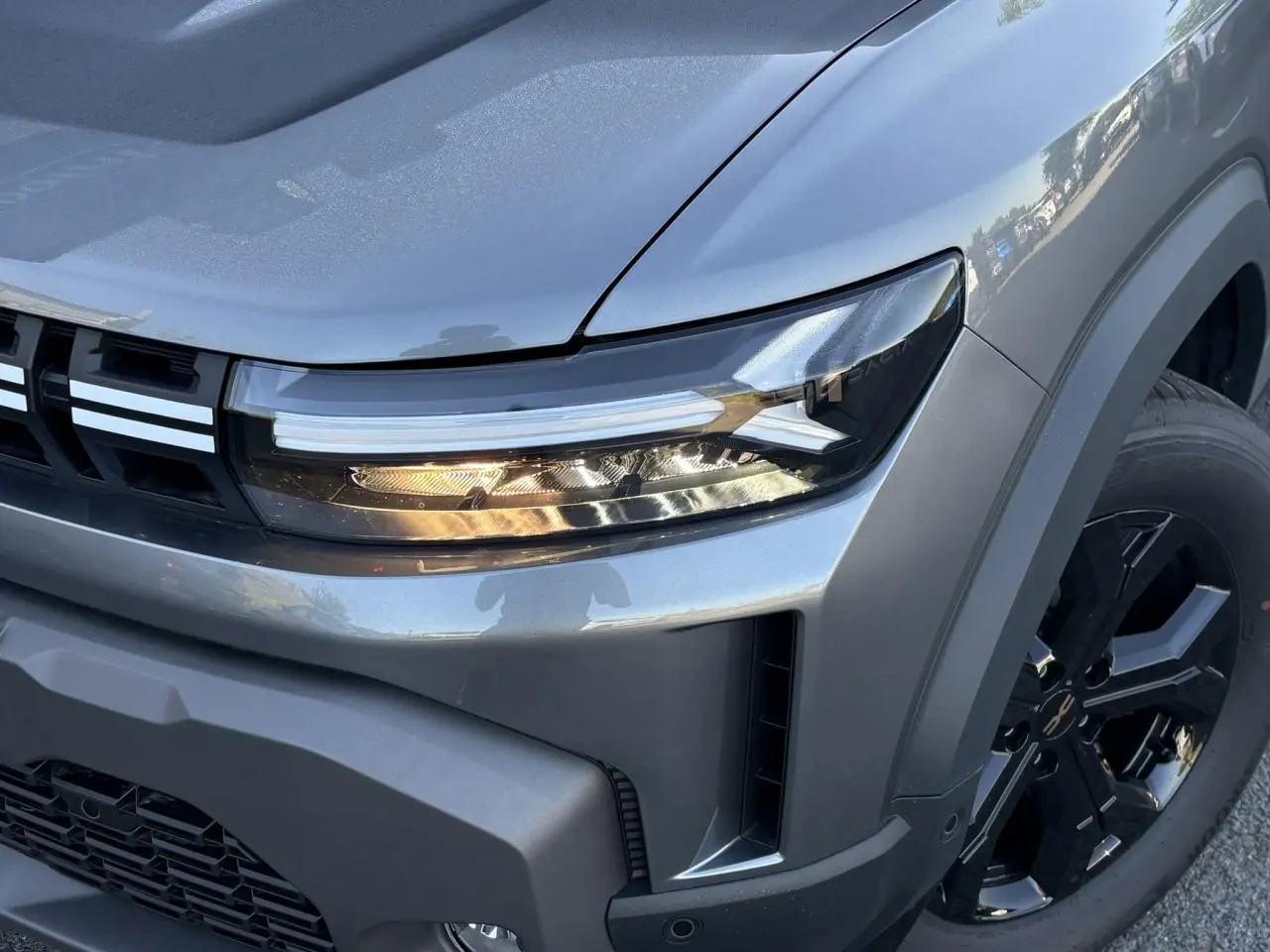 Gros plan sur l'avant droit du Dacia Duster gris schiste, mettant en valeur le phare LED et la jante alliage noire.