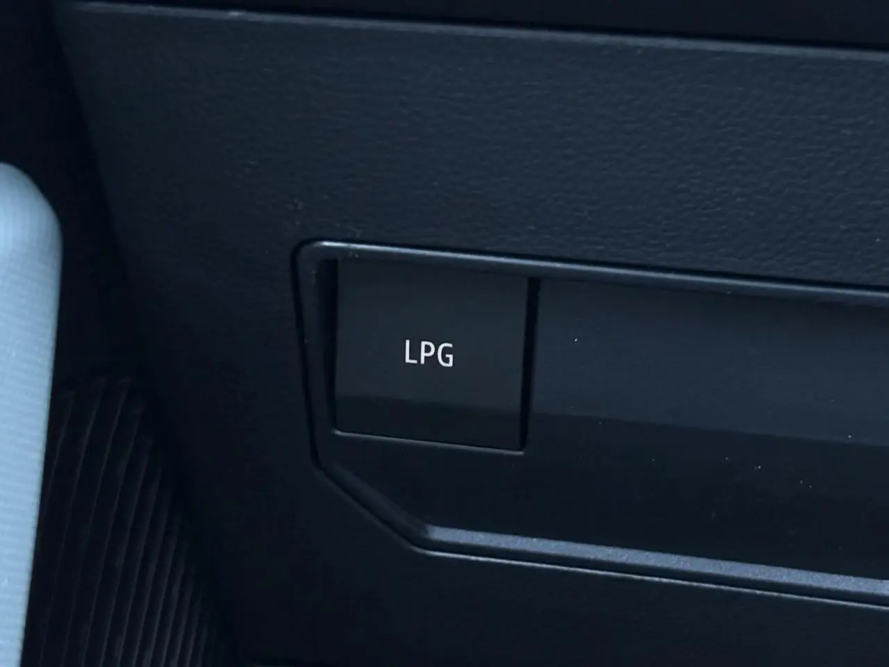 Gros plan sur le bouton LPG noir dans l'habitacle du Dacia Duster gris, indiquant la bicarburation GPL.