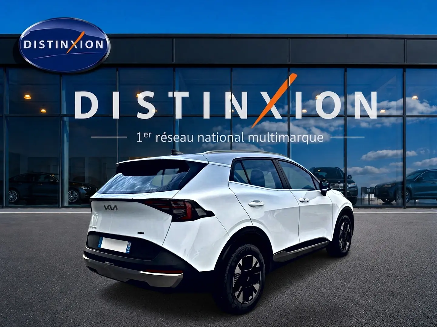 Vue 3/4 arrière droite d'un KIA SPORTAGE blanc 2026 avec jantes noires et feux arrière LED, devant une vitrine Distinxion.