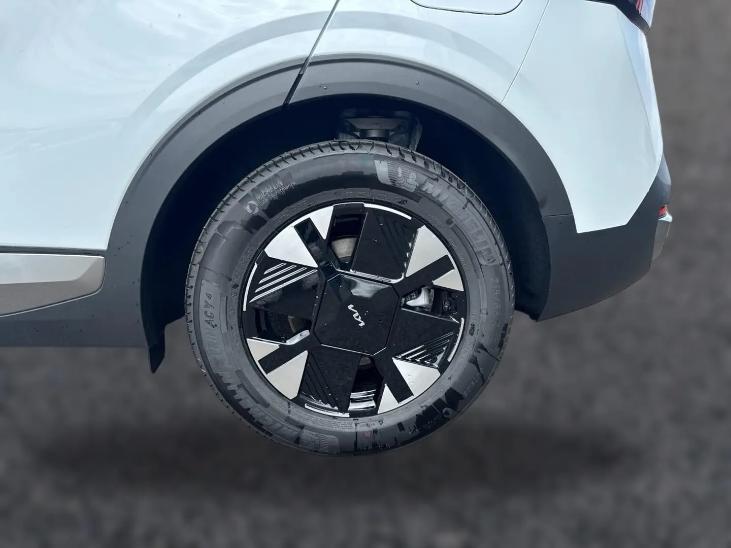 Gros plan sur la roue arrière droite blanche du Kia Sportage 1.6 hybride 239 avec jante alu noire et argentée au design géométrique.