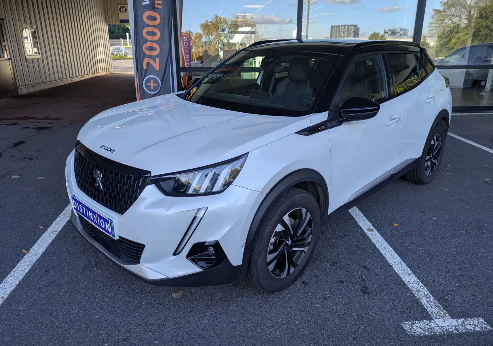 Peugeot 2008 GT blanc nacré en 3/4 avant droit, toit noir et jantes bi-ton visibles sur parking extérieur.
