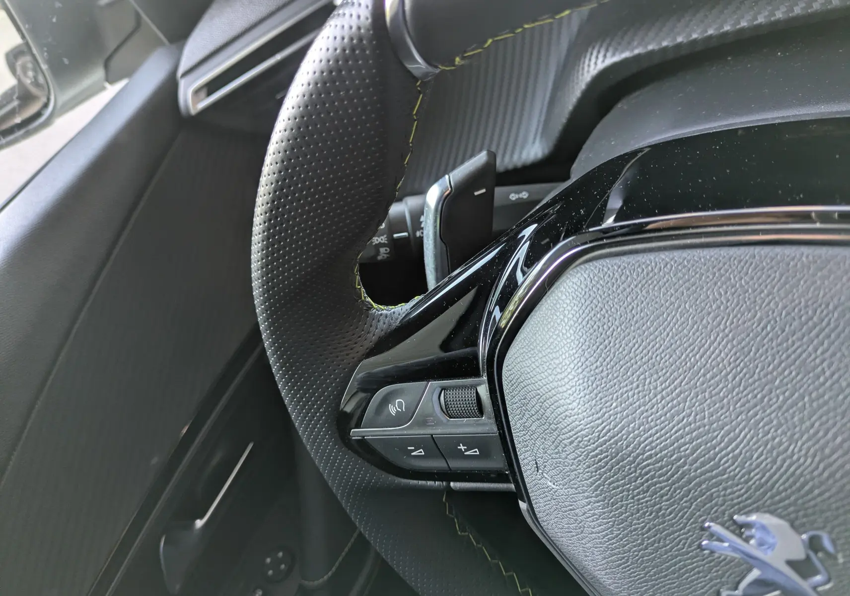 Gros plan sur le volant perforé avec surpiqûres jaunes du Peugeot 2008 GT blanc nacré, montrant les commandes intégrées.