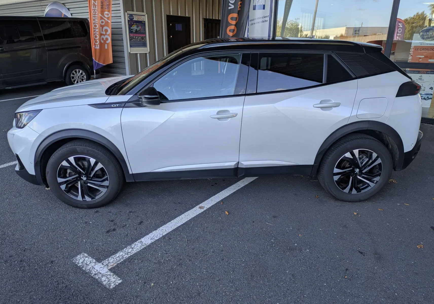 Peugeot 2008 GT blanc nacré en profil côté gauche, toit noir contrastant et jantes alliage bicolores visibles.