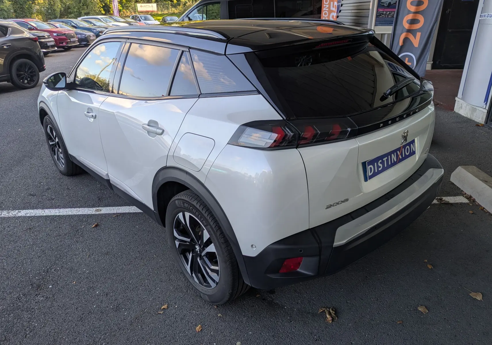 Vue 3/4 arrière droite d’un Peugeot 2008 GT blanc nacré avec toit noir et jantes bi-ton, stationné en extérieur.
