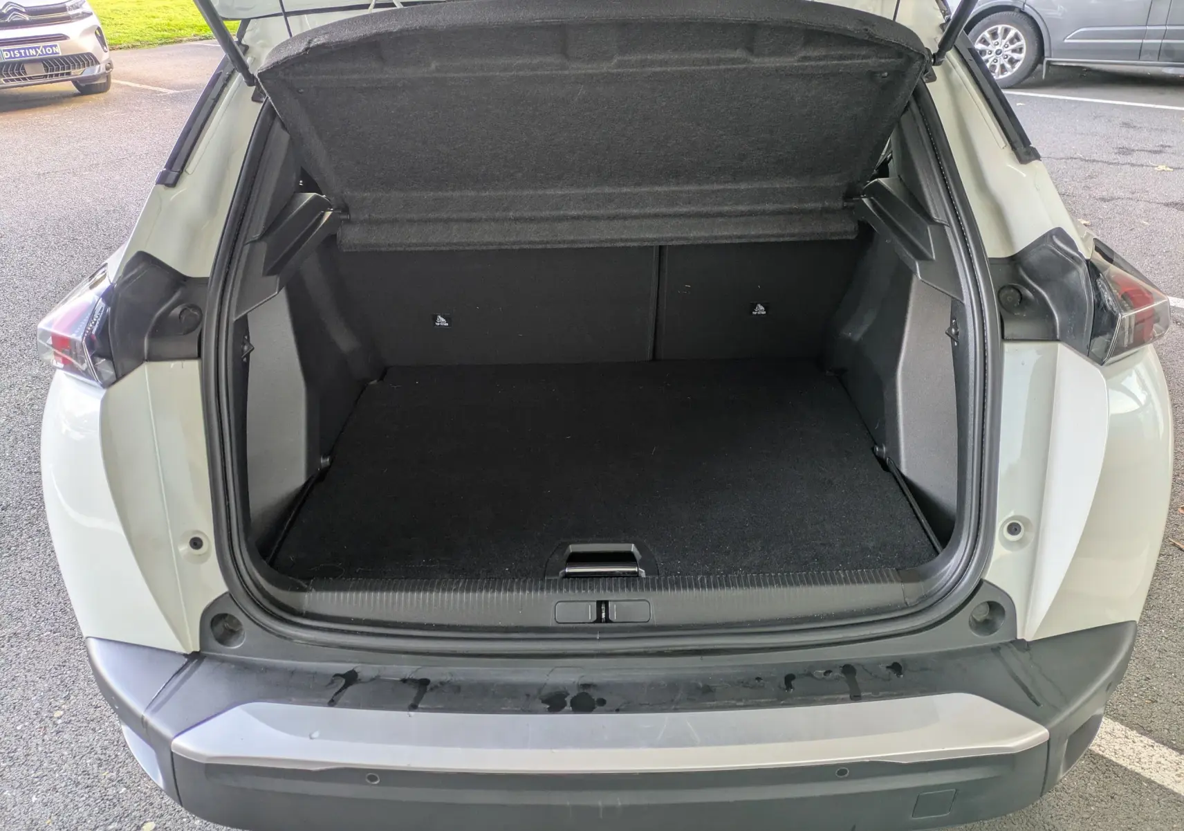 Coffre ouvert vu de l'arrière d'un Peugeot 2008 GT blanc nacré, montrant un espace de chargement vide et propre.