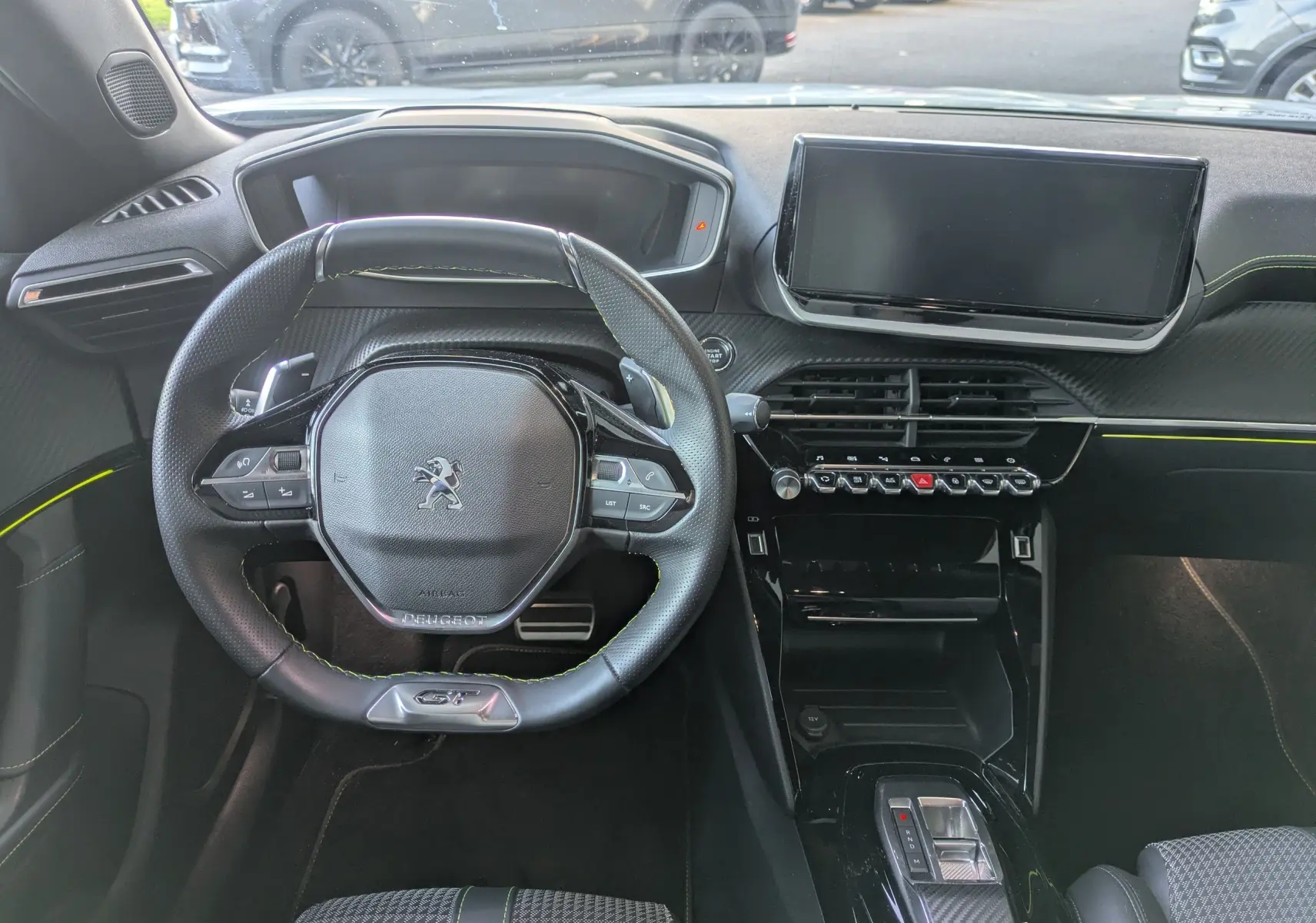 Vue intérieure du poste de conduite du Peugeot 2008 GT 2022, volant compact avec surpiqûres vertes et écran tactile central.