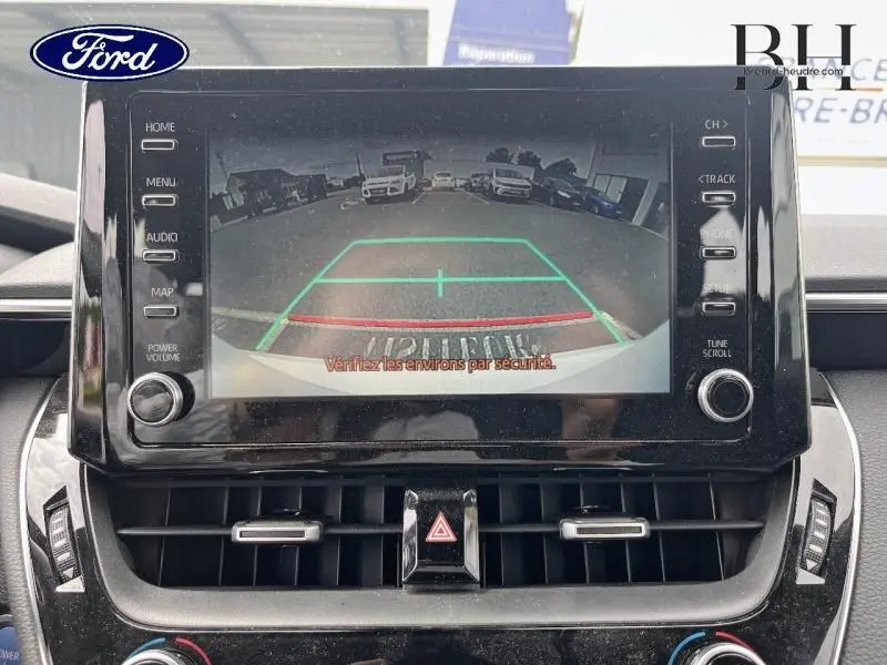 Écran tactile affichant la caméra de recul d'une Toyota Corolla blanche vue de l'arrière en stationnement.