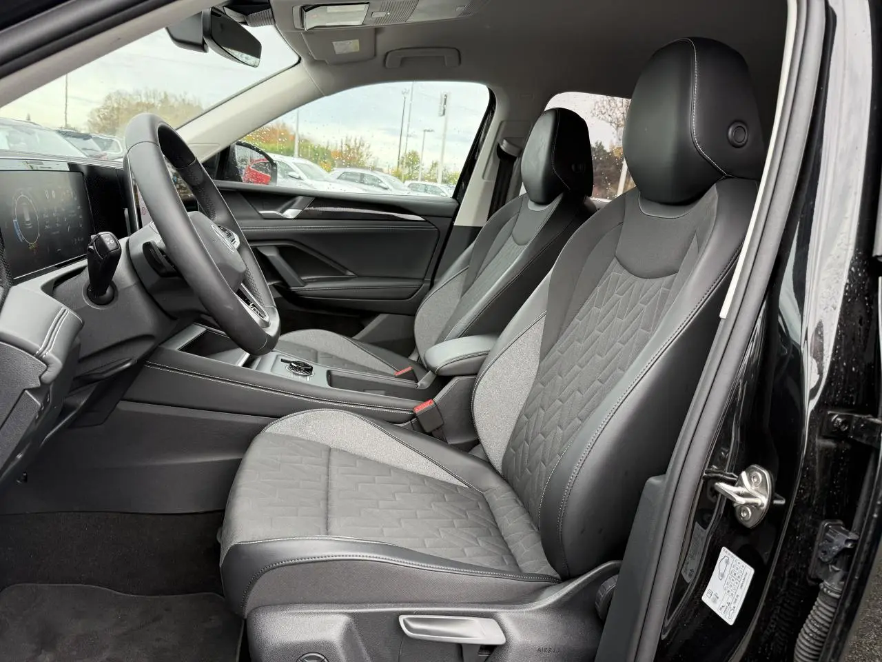 Vue intérieure côté conducteur du Volkswagen Tiguan 2025 noir grenadille, sièges tissu et cuir gris, tableau de bord digital.