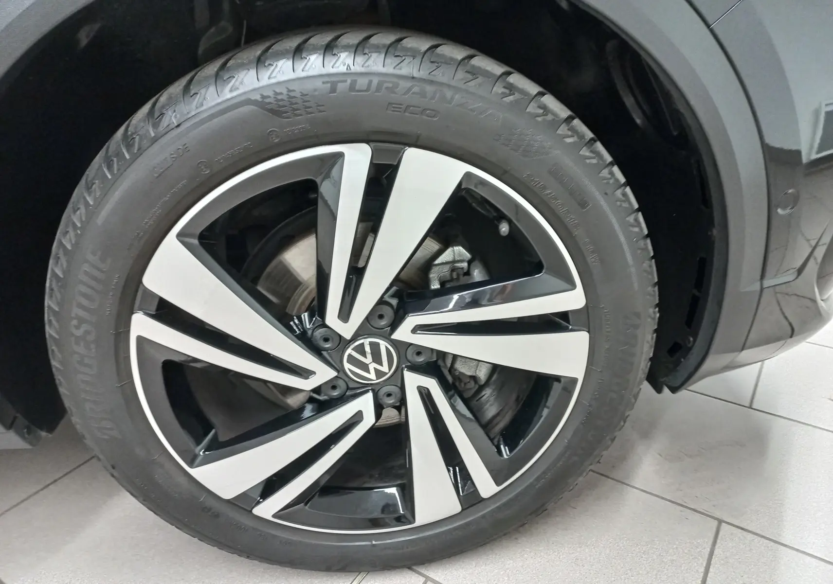 Gros plan sur la roue avant droite du Volkswagen T-Roc noir intense, avec jante alliage bicolore et pneu Bridgestone.
