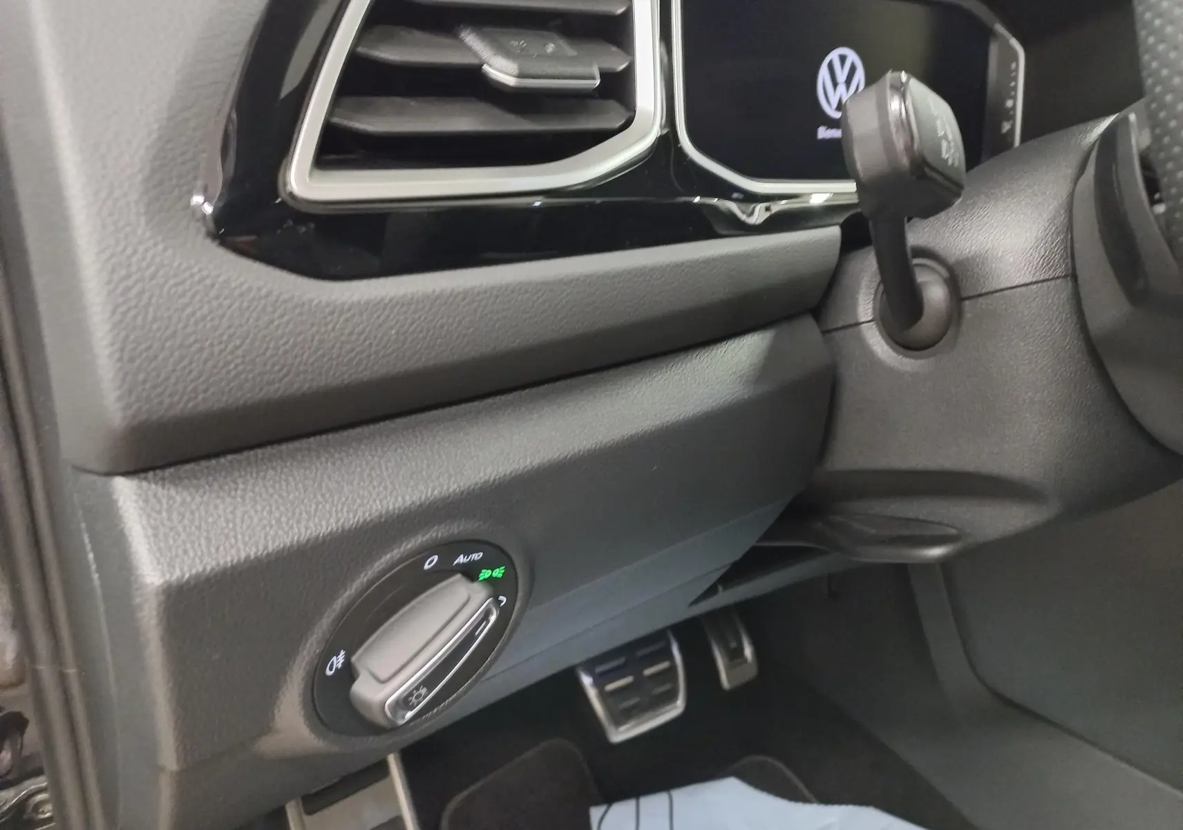 Détail intérieur côté gauche du tableau de bord du Volkswagen T-Roc 2025 avec commandes d'éclairage et aérateurs noirs.