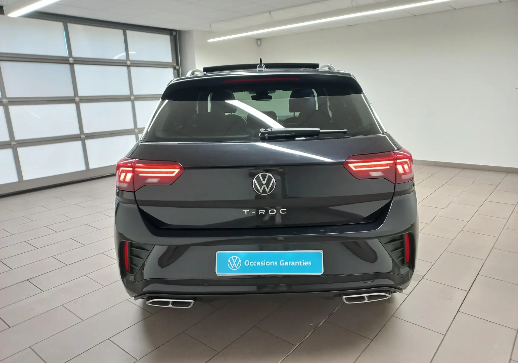 Vue arrière d'un Volkswagen T-Roc noir intense avec feux LED allumés et double sortie d'échappement visible en intérieur.