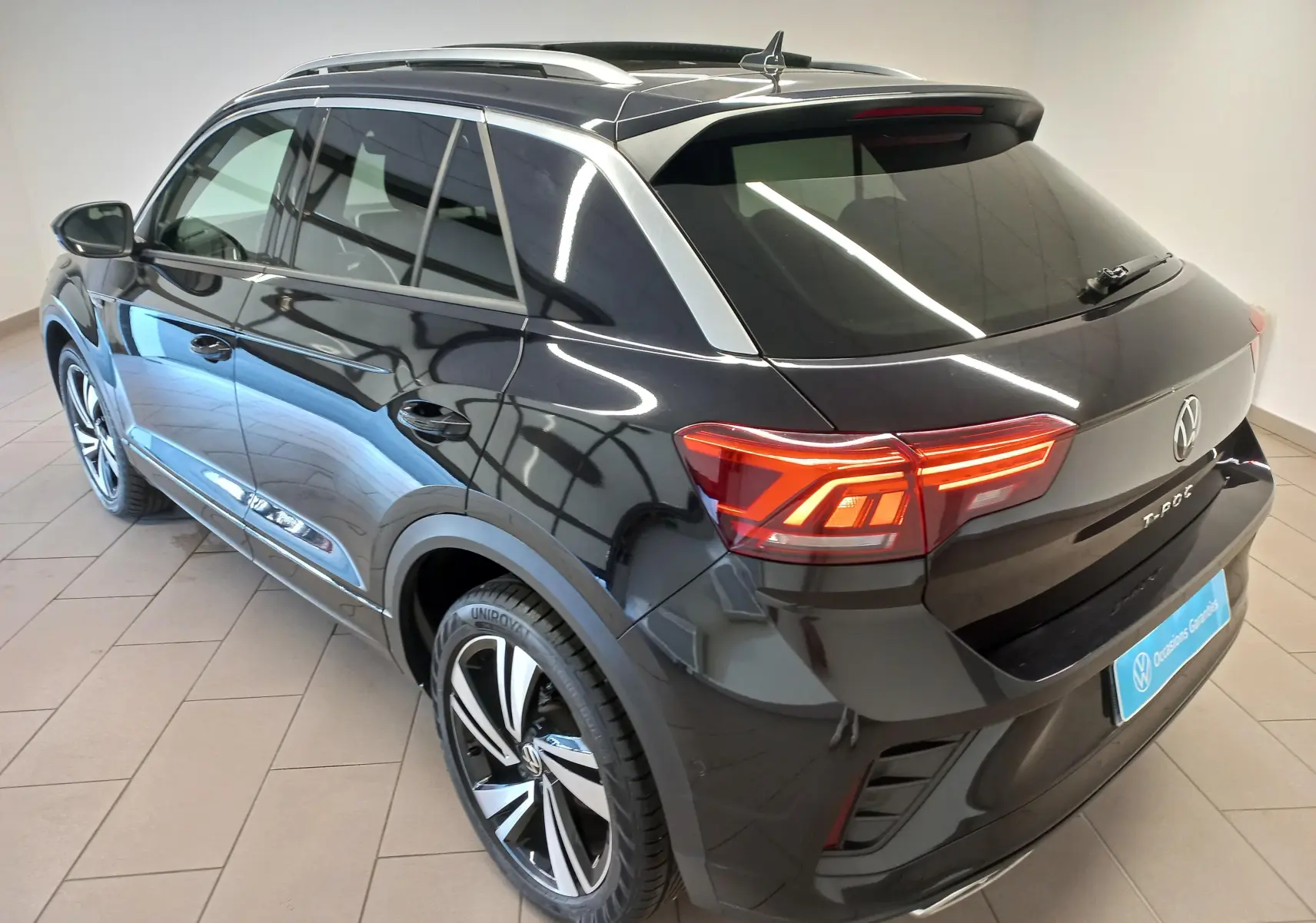 Vue 3/4 arrière droite du Volkswagen T-Roc noir intense avec toit ouvrant et feux arrière LED allumés.