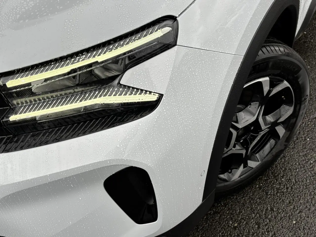 Gros plan sur l'avant droit blanc Okénite du Citroën C5 Aircross 2025, mettant en valeur le phare LED et la jante alliage bi-ton.