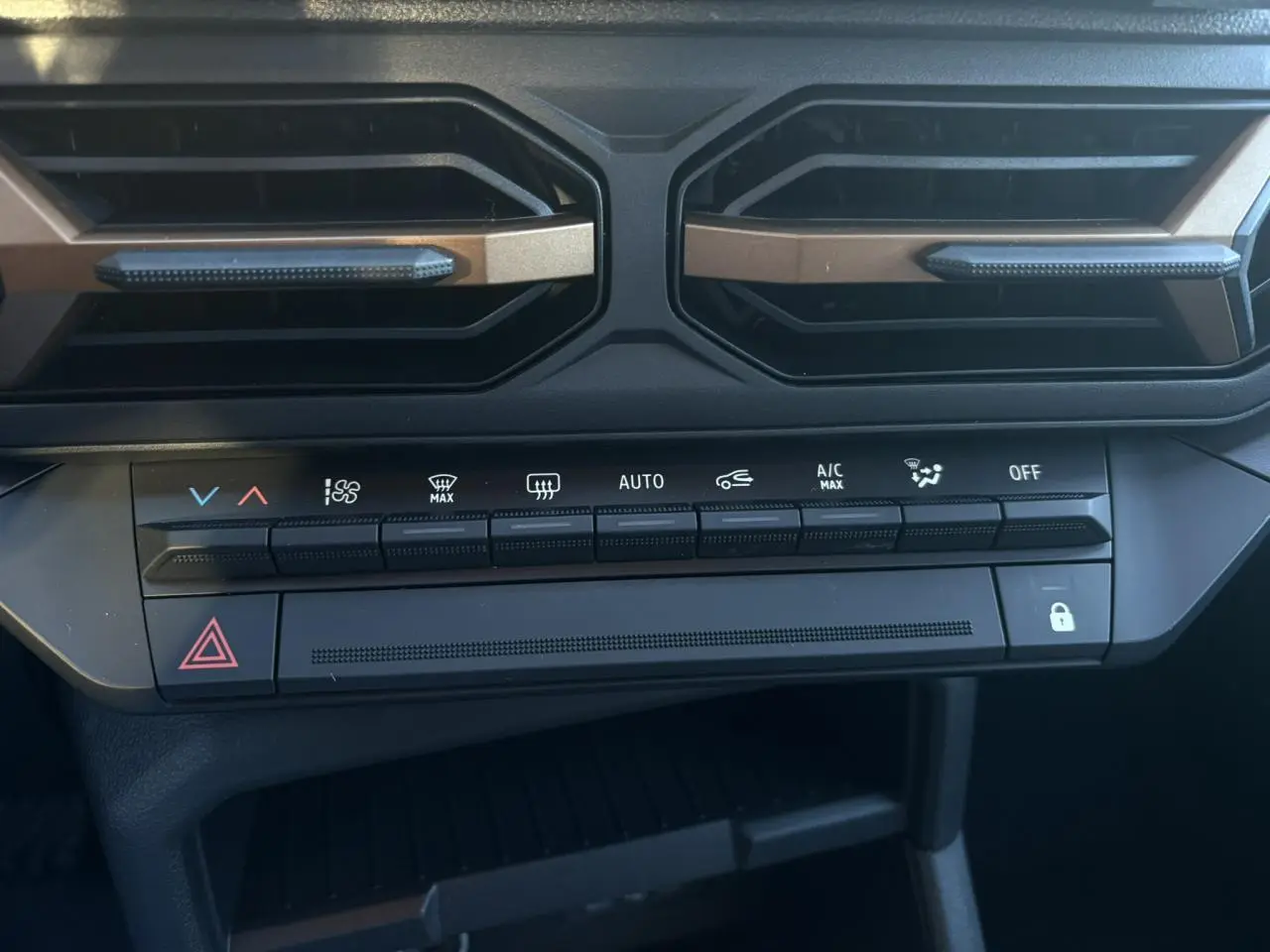 Vue rapprochée de la console centrale du Dacia Duster 2026, boutons de climatisation et aérateurs noirs avec inserts bronze.