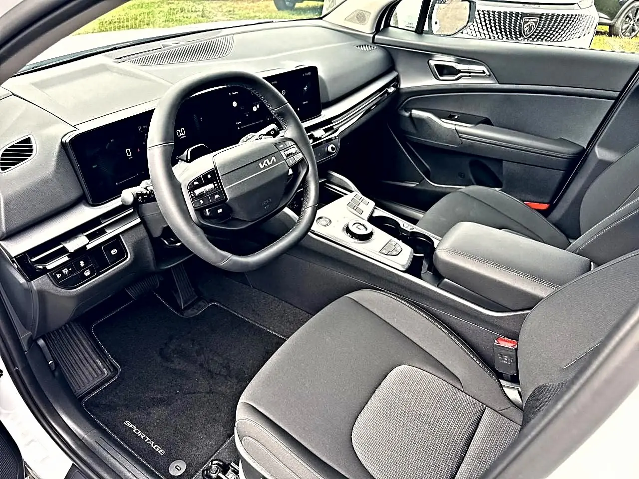 Vue intérieure côté conducteur du Kia Sportage 1.6 hybride blanc, avec volant multifonction et écran tactile large.