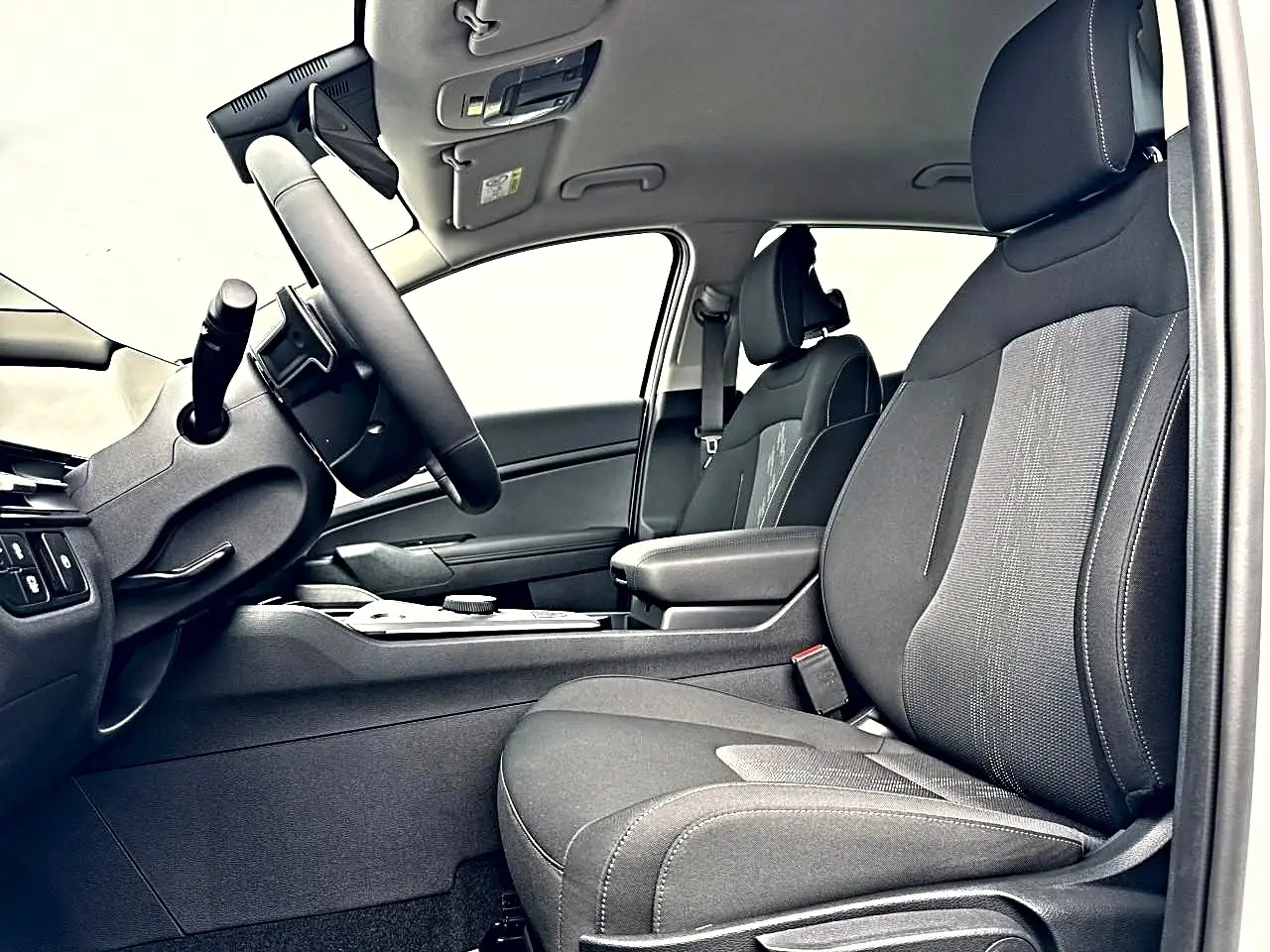 Vue intérieure côté conducteur du Kia Sportage 1.6 hybride 239 active, sièges noirs et accoudoir central avec rangement.