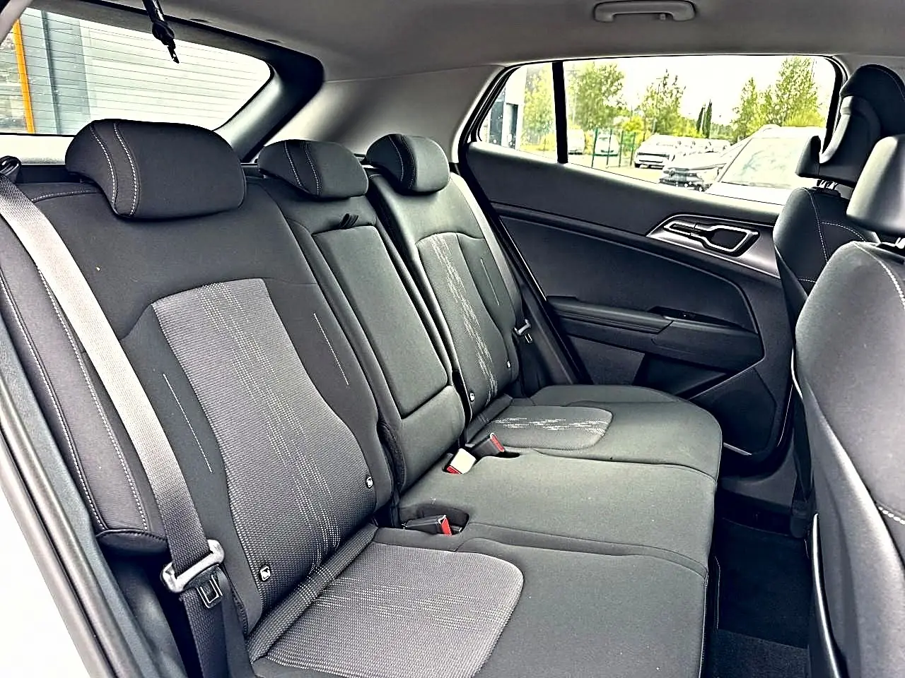Vue latérale droite de la banquette arrière noire du Kia Sportage 1.6 hybride 239 active avec appuie-têtes et ceintures visibles.
