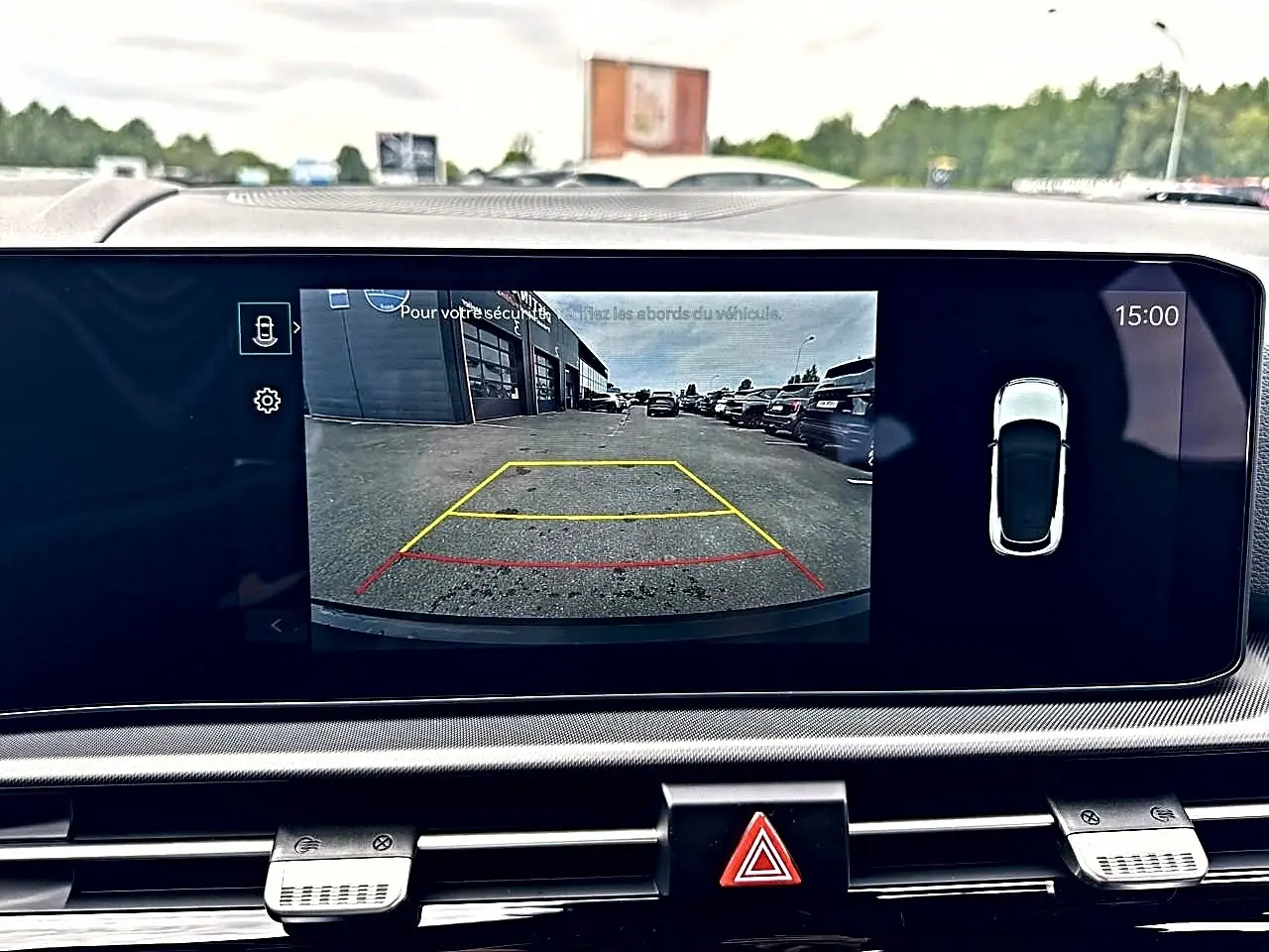 Écran tactile intérieur montrant la caméra de recul d’un KIA SPORTAGE blanc hybride, vue arrière en stationnement.