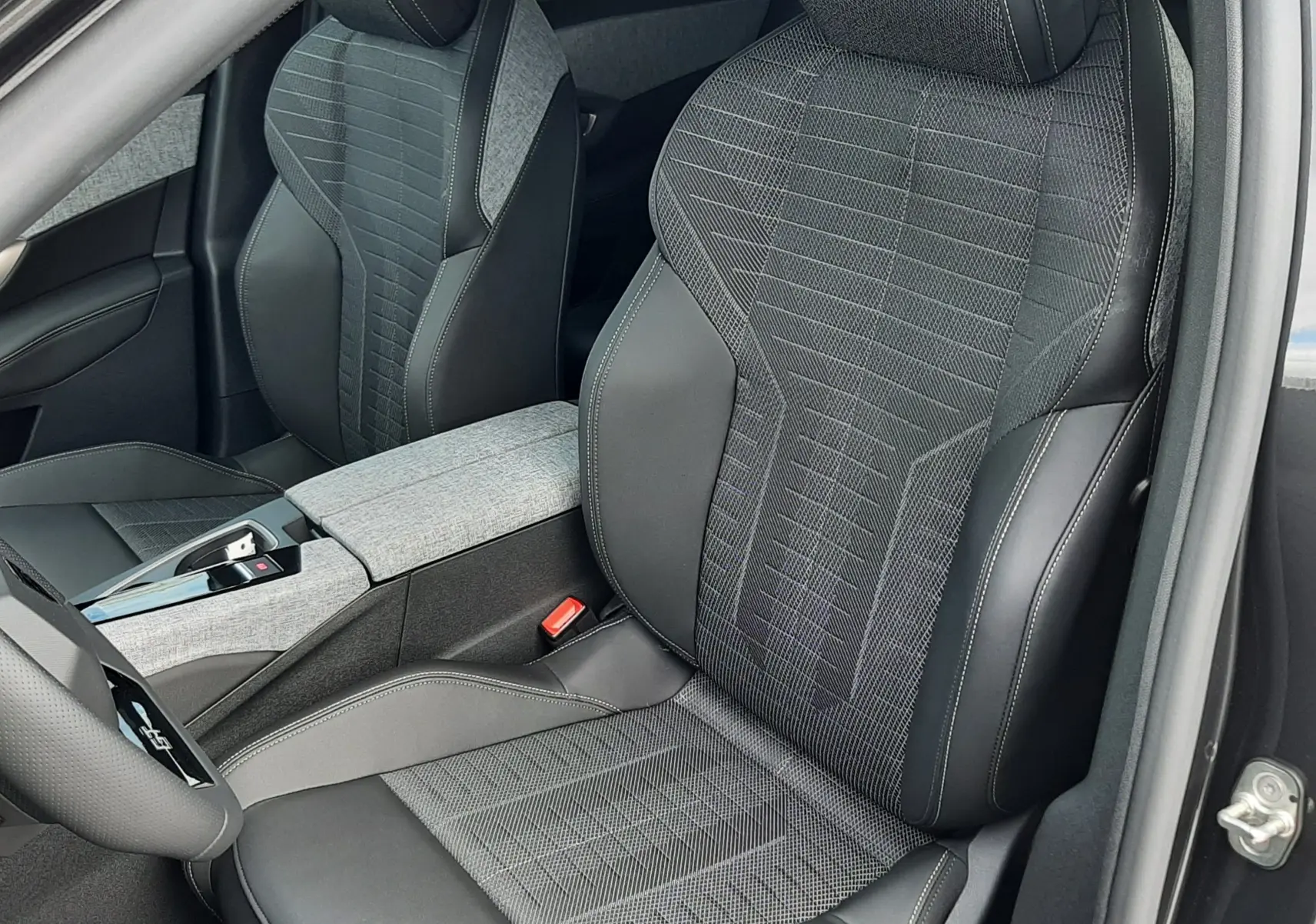 Vue intérieure rapprochée des sièges avant du Peugeot 3008 gris titane, avec sellerie mixte tissu et cuir noir et logo brodé sur appuie-tête.