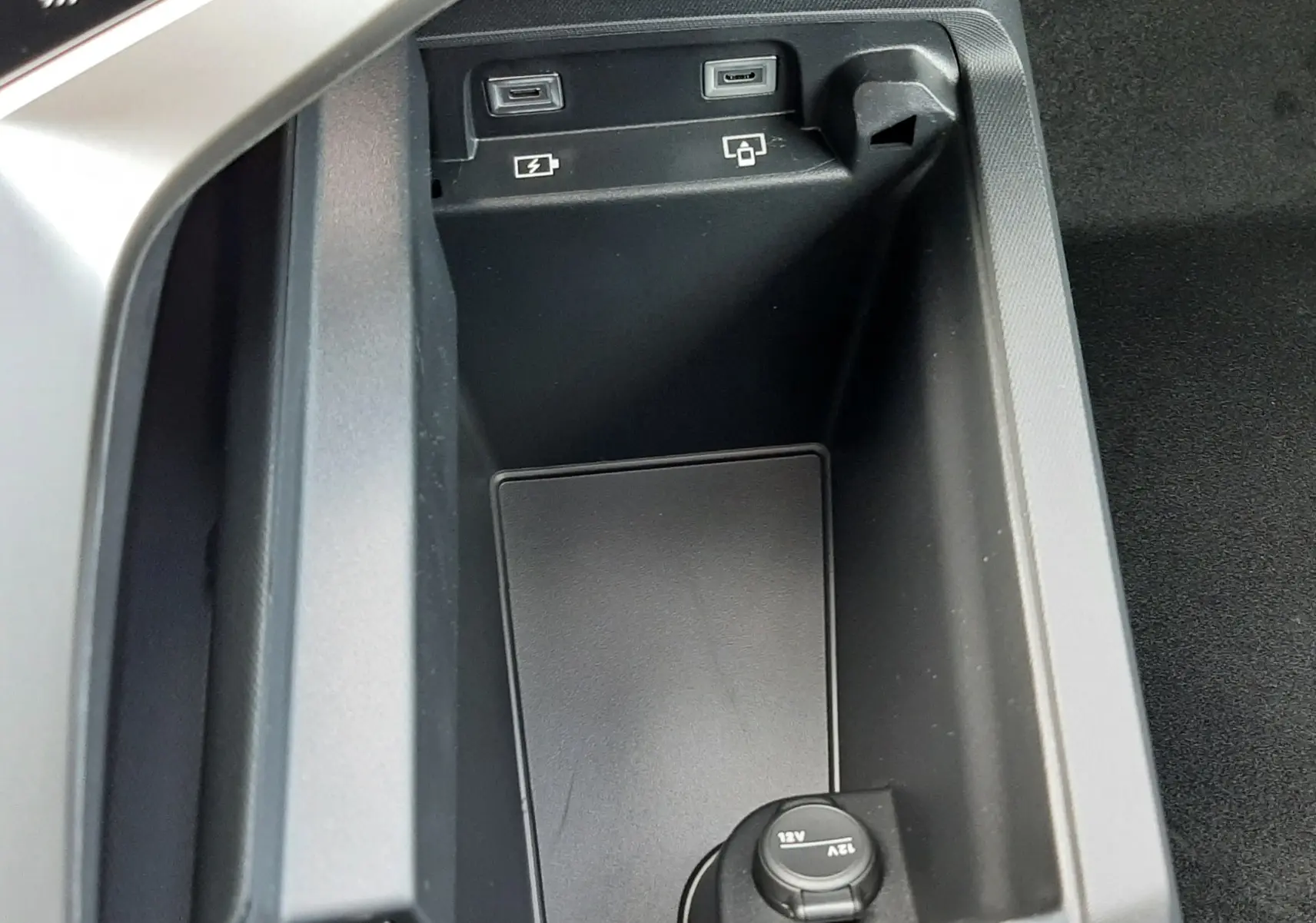 Gros plan sur la console centrale noire du Peugeot 3008 1.2 Hybrid, montrant prises USB et prise 12V.