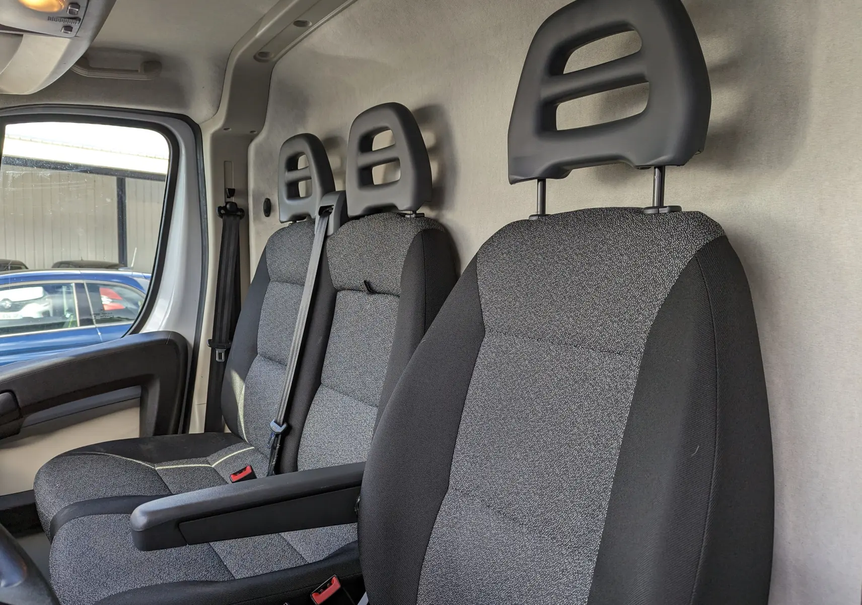 Vue intérieure côté conducteur du FIAT Ducato Fourgon blanc 2019, sièges tissu gris avec appuie-têtes ajourés.