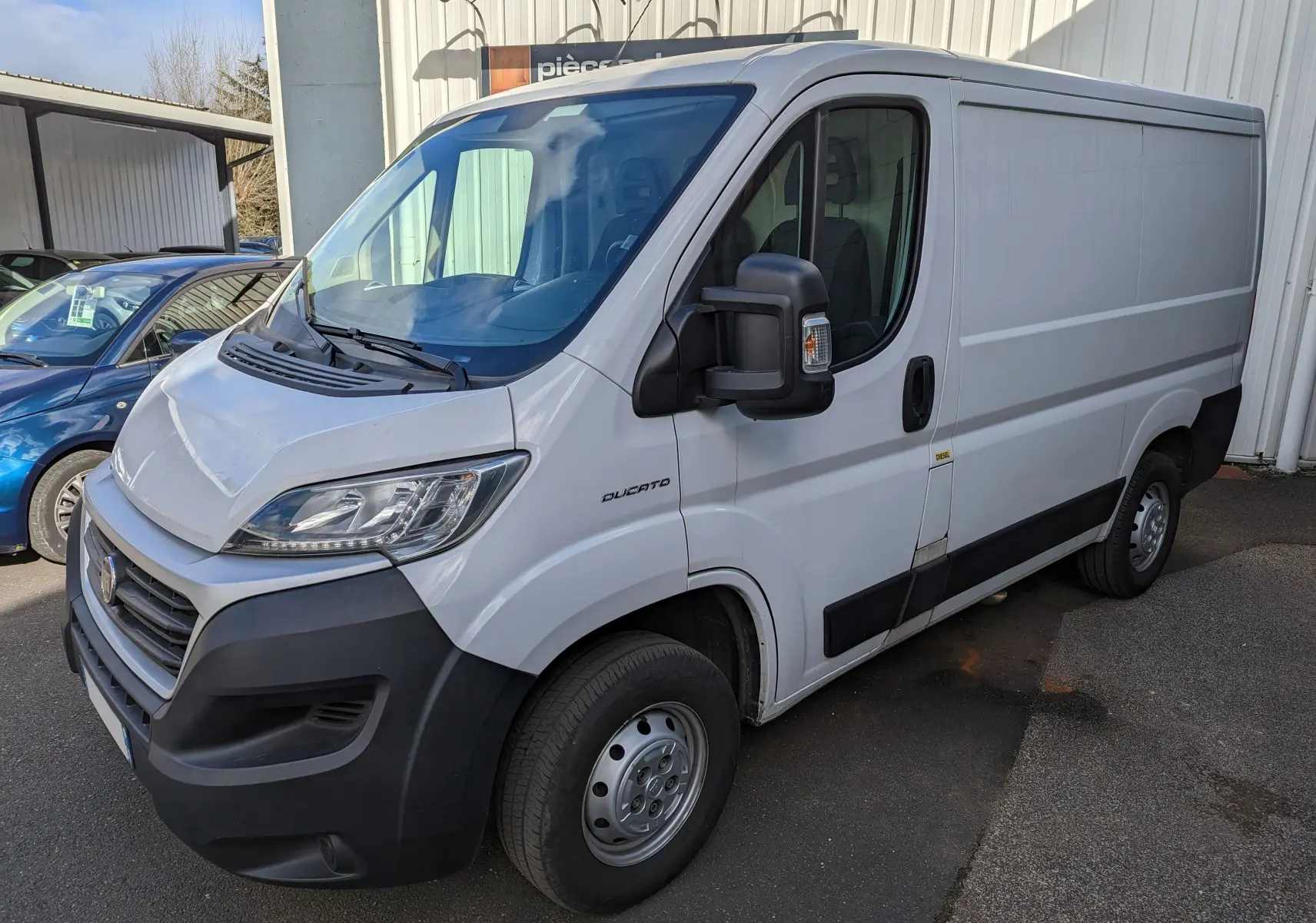 Vue 3/4 avant droit d'un FIAT Ducato Fourgon blanc de 2019 avec rétroviseur noir et jantes acier simples.