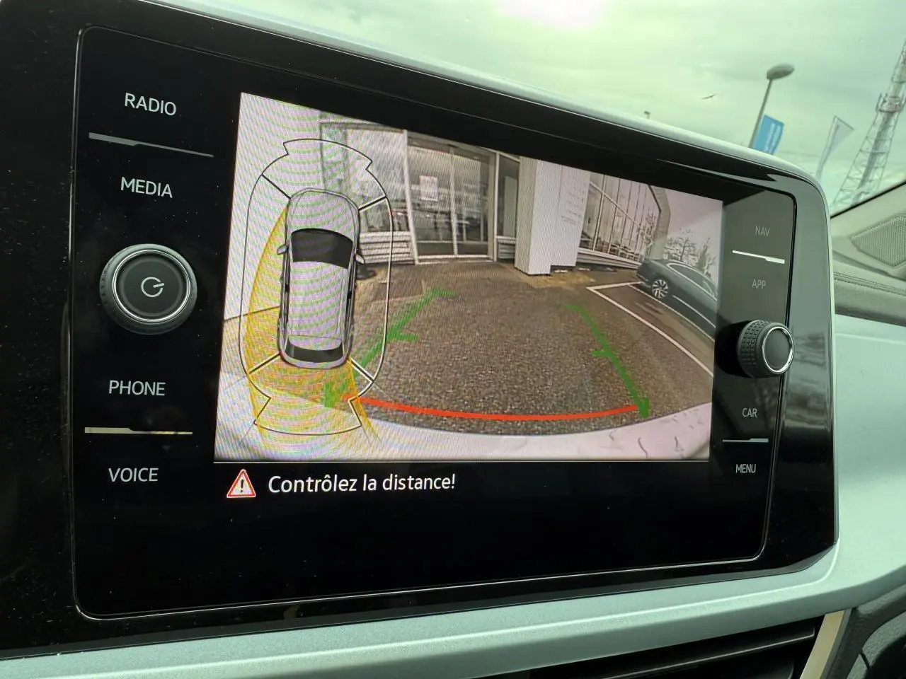 Vue de la caméra de recul du Volkswagen T-Roc argent pyrite métallisé montrant l'arrière et un parking adjacent.