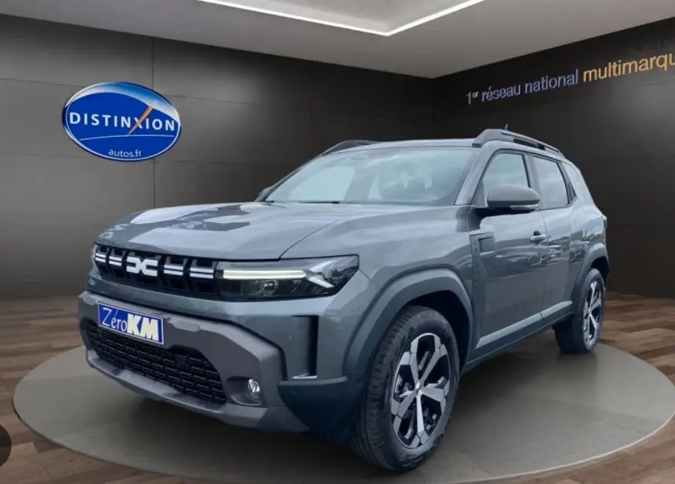 Vue 3/4 avant droit du Dacia Duster 1.8 Hybrid 155 Journey en gris schiste métallisé avec jantes bi-ton et calandre distinctive.