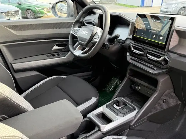 Vue intérieure côté conducteur du Dacia Duster 1.8 Hybrid 155 Journey avec sellerie spécifique et écran tactile central.