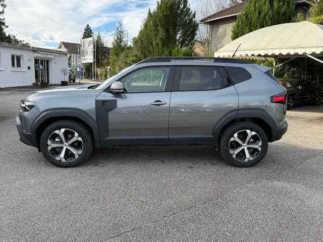 Vue de profil côté gauche du Dacia Duster 1.8 Hybrid 155 Journey en gris schiste métallisé avec jantes bi-ton et sellerie spécifique.